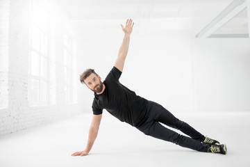 Fototapeta premium Handsome man in the black sportswear holding plank on the floor in the white gym interior