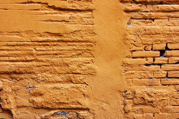 Old , yellow destroyed plaster at a brick wal