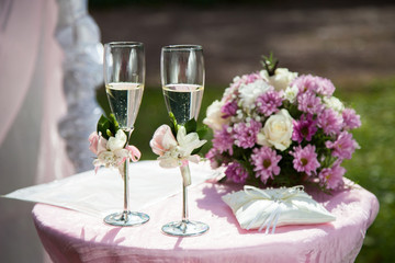 Two decorated wineglasses with champagne, ring pillows and weddi