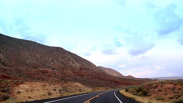 A car drives at Highway, cutting the desert of Arizona with and indescribable beauty. The road travels on painted desert, through a lava field and opens up to the State Mountain and Red Mountain.