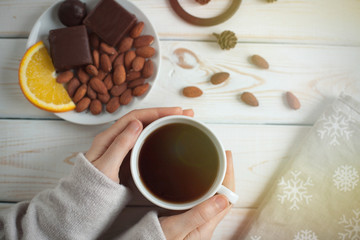 Women's hands holding a cup of coffee on a wooden table. top view.