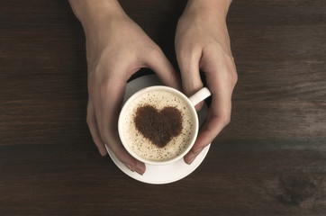 Female hand hold coffee cup with heart shape on wooden table