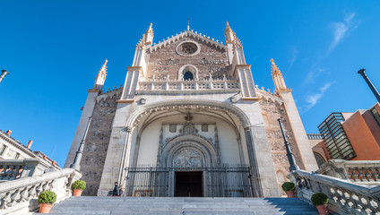 Bright, blue sky, sunshine on beautiful old stone & masonry cathedral.  Steps leading to spear-tipped wrought iron gates at the front.  Worn stonework on walkway railings.