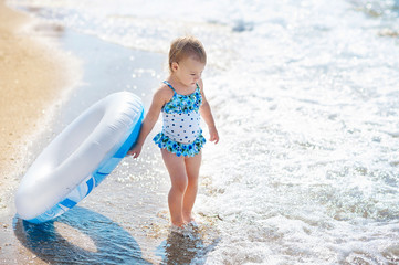 Little girl in swim suit with swimming circle ready to go into the sea at early sunset. Summer fun.
