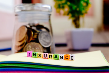 conceptual image with INSURANCE word block on note pad.coin in glass jar with soft focus background