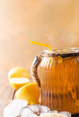 Lemon ice tea on brown wooden table with lemons around. Iced tea with lemon slices and mint on rustic background
