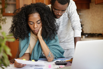 Stressed African couple having many debts trying to cut their domestic expenses to save money and pay off loan in bank. Worried wife holding piece of paper and reading notification about eviction