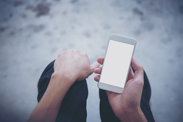 Mockup image of a man sitting on the street and holding white mobile phone with blank white screen   