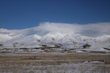 Winter panorama view in a sunny day. Armenian mountains partially covered with snow and clouds on the background