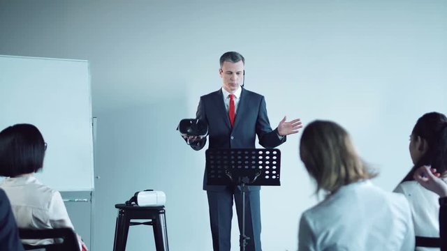 Adult businessman standing at the board and presenting the vr headset to the colleagues.