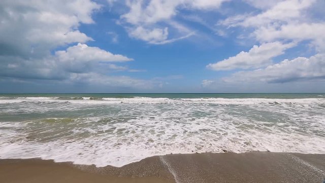 Loop features foamy gentle waves breaking on a sandy beach under a beautiful cloudy blue sky at Cocoa Beach, Florida.
