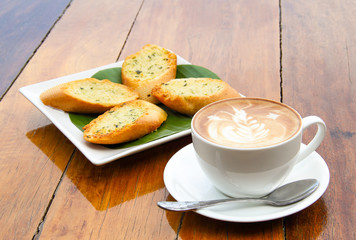 Cup of latte coffee and homemade garlic herb bread on table