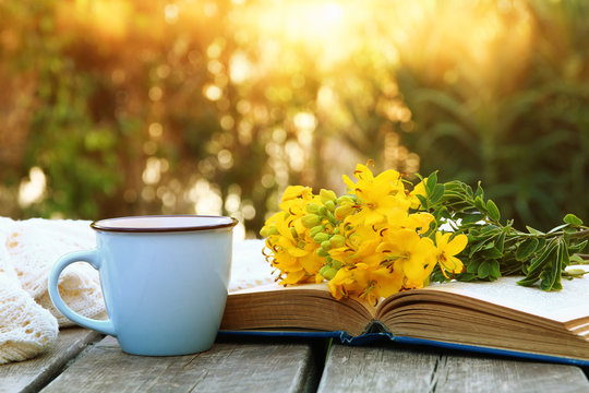old book, cup of coffee next to field flowers