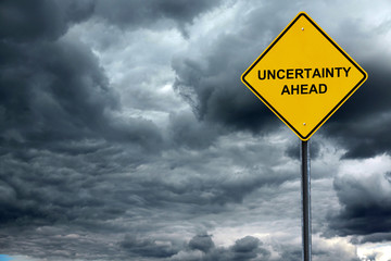 road warning sign with text uncertain ahead in front of storm cloud background