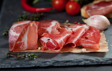 Ham , cherry tomatoes, red pepper and herbs on black stone slate board.