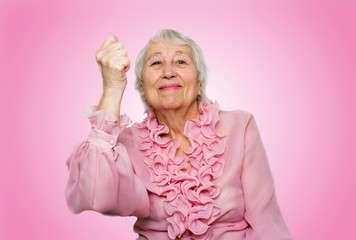 portrait of a cheerful senior woman gesturing victory over pink 