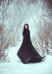 Gothic woman fantasy witch. sexy girl demon walks in forest. wearing a long, black traveling cloak....