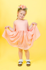 beautiful young pretty girl in beige dress with wreathe on her had in photo studio on yellow background