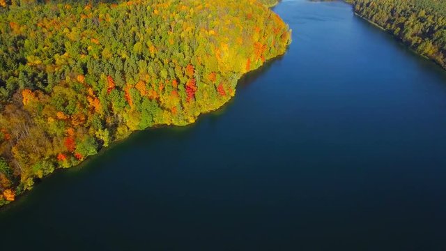Autumn nature aerial landscape flight over forest lake and brightly colored trees.