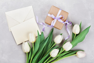 Spring tulip flowers, gift box and paper card on gray stone table top view in flat lay style. Greeting for Womens or Mothers Day.