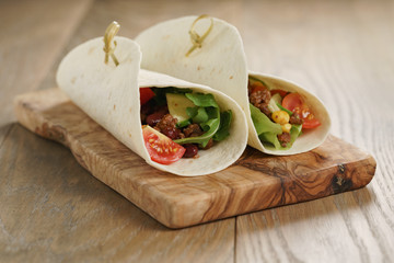 tortilla wrap sandwiches with beef and vegetables on olive board, closeup photo with shallow focus