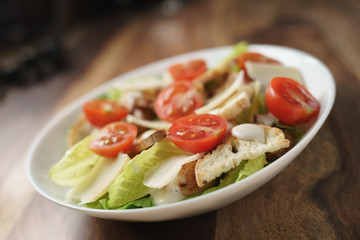 fresh caesar salad with chicken and cherry tomatoes on wood table, shallow depth of field