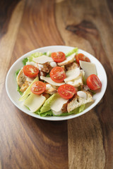 fresh caesar salad with chicken and cherry tomatoes on wood table, shallow depth of field
