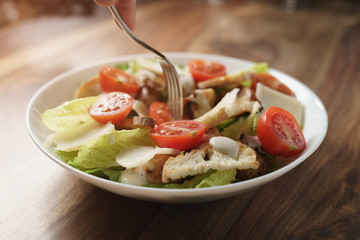 eating caesar salad with chicken and cherry tomatoes on wood table, shallow depth of field