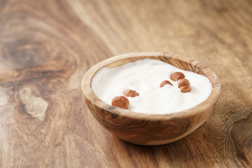 homemade yogurt with hazelnuts in wood bowl on wooden table, shallow focus