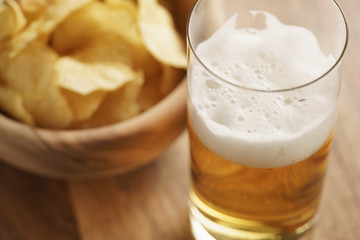 glass of lager beer with potato chips on wooden table, focus on beer