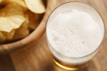 glass of lager beer with potato chips on wooden table, focus on beer