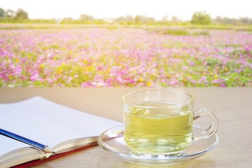 cup of tea and open notebook on wooden with multicolored flower field background; copy space for text.