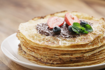 fresh blinis or crepes with melted dark chocolate, berries and sugar powder, shallow focus