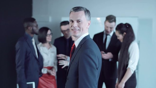 Joyful adult man looking back to colleagues and looking at camera. 4K middle shot