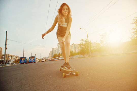 Beautiful young girl with tattoos riding on his longboard on the road in the city in sunny weather. Extreme sports. Rear view of motion