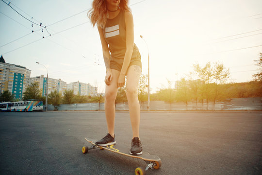 Beautiful young girl with tattoos riding on his longboard on the road in the city in sunny weather. Extreme sports. Rear view of motion