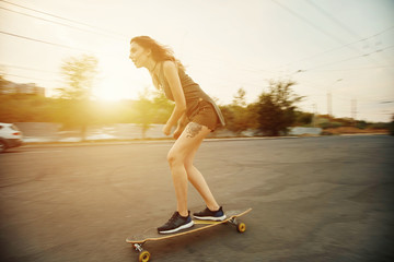 Beautiful young girl with tattoos riding on his longboard on the road in the city in sunny weather. Extreme sports. Rear view of motion