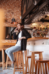 Vertical image of bearded man sitting on bar with phone