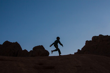 child silhouette running over the rocks in the desert at sunset