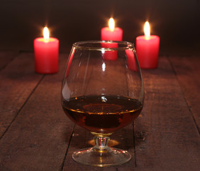 glass of wine or cognac and red candle on a wooden background.