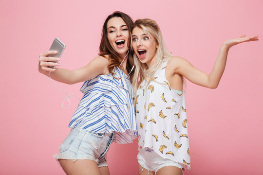 Two cheerful young women listening to music and talking selfie