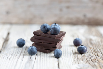 Dark chocolate stack and fresh organic blueberries on wooden table. Natural light, selective focus. 