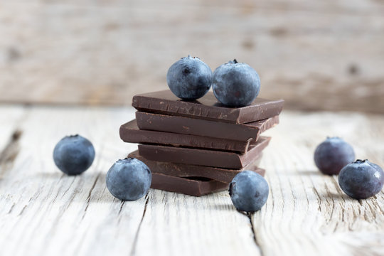 Dark chocolate stack and fresh organic blueberries on wooden table. Natural light, selective focus. 