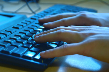 Two hands typing on a keyboard on blue light