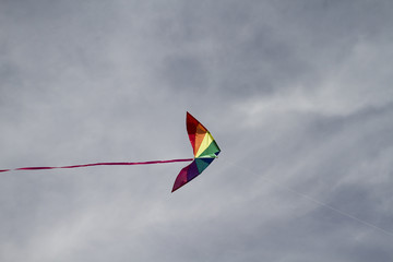 Kite of rainbow colors on a blue sky with light white clouds