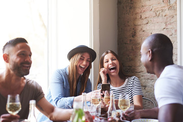 Friends laughing at something on phone at dinner