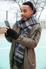 Concentrated african man using smartphone outdoors in autumn