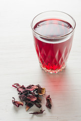 Hibiscus tea in a glass mug on a wooden table among rose petals and dry tea custard