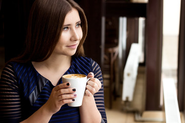 The girl in the blue dress sitting with a cup of cappuccino and looking out the window