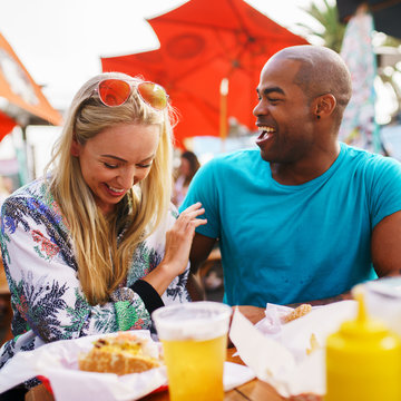 Playful Couple Eating At Outdoor Restaurant With Burgers And Beer